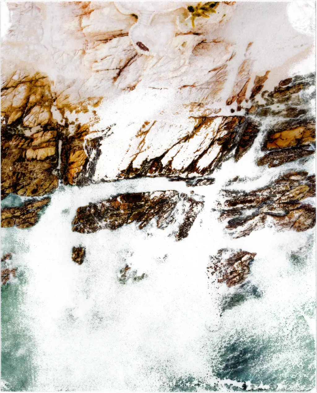 An aerial image of a rocky mediterranean coastline printed on acetate and bathed in disinfectant. The darker areas of the print have a higher concentration of ink resulting in that area withstanding the disinfectant longer. This means most of the light greenish blue hues of the ocean have washed away while the darker tones of the rocky coastline have remained. Some of the most ink rich areas of the image have glooped and glopped together during the disinfectant bath causing them to coagulate into messy strands of dark tones, only holding onto the acetate at the very ends.