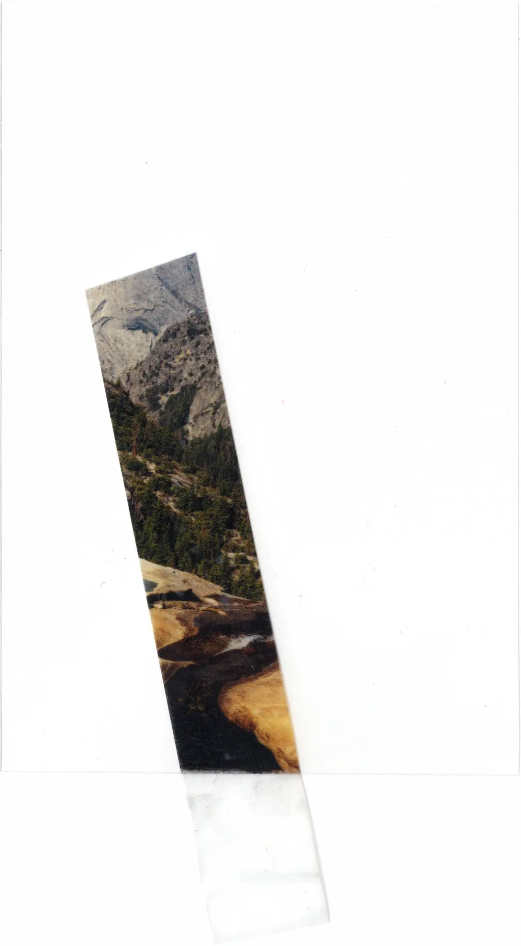 A scenic view of a river snaking down a mountainous region printed on acetate, a single piece of transparent scotch tape masking said river. The disinfectant has washed away everything but what was under the protection of the tape.